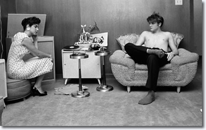 After having taken a shower, and still bare chested, Elvis has his high school sweetheart, Barbara Hearn, listen on the phonograph to the acetate disc with cuts of his songs from the New York recording session. 1034 Audubon Drive, Memphis, Tenn. July 4, 1956. (Photo © Alfred Wertheimer. All rights reserved.)